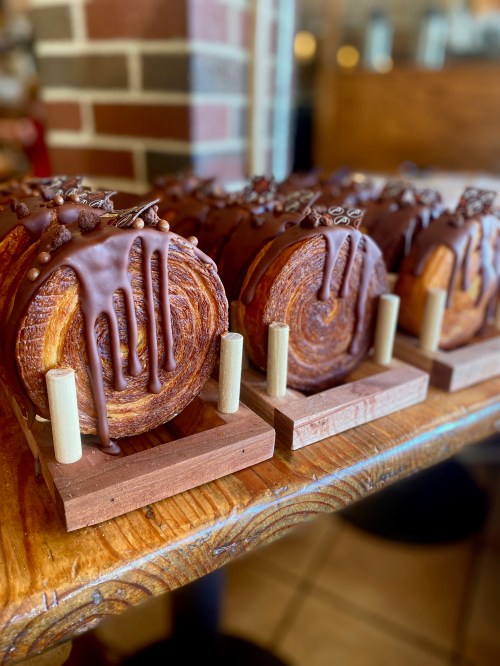 Three chocolate-drizzled pastries displayed on wooden stands, showcasing a rich, swirled texture.