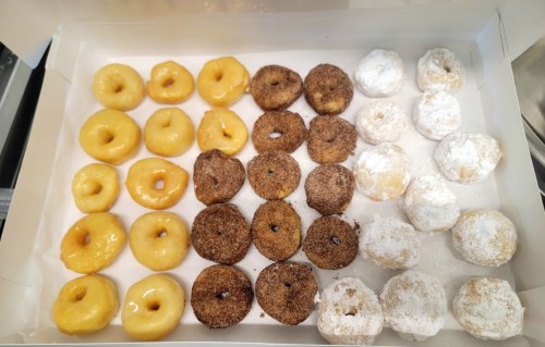 A box of assorted donuts: glazed, cinnamon sugar, and powdered sugar varieties arranged in rows.