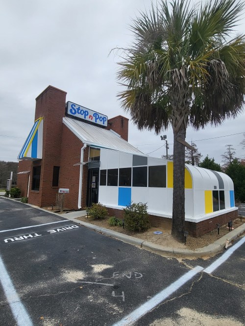 A fast-food restaurant named "Stop n Pop" with a colorful exterior and a palm tree in front.