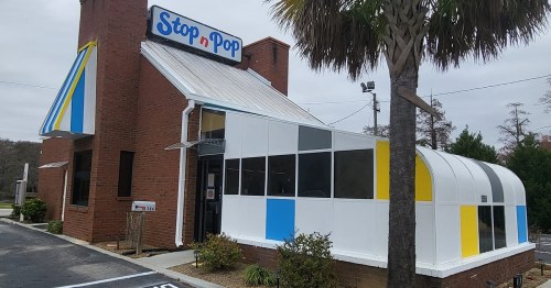 Exterior of a brick building with a colorful awning, featuring large windows and a sign that reads "Stop n Pop."