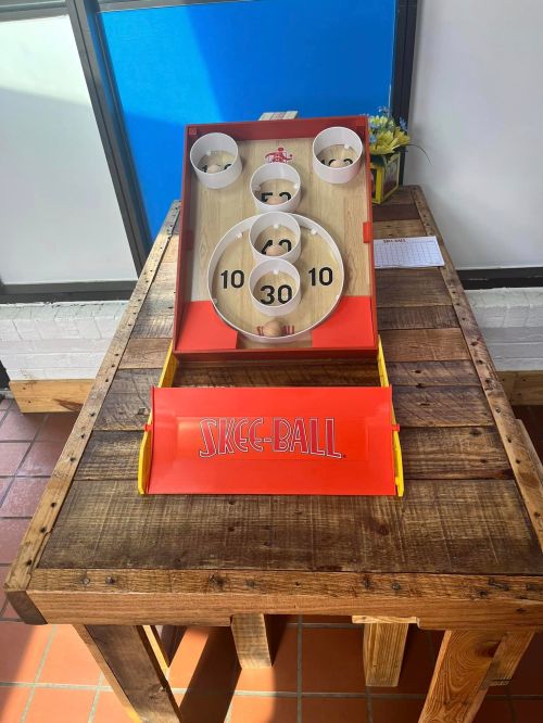 A skee-ball game on a wooden table, featuring numbered holes and a bright red design.