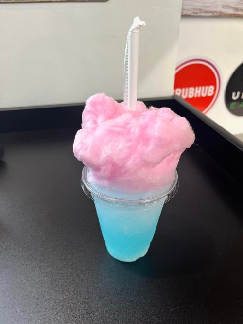 A clear cup filled with blue liquid topped with fluffy pink cotton candy and a straw.
