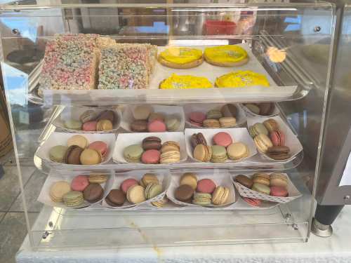 A display case filled with colorful macarons, cookies, and rice crispy treats.