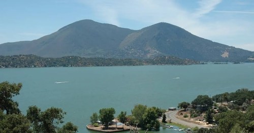 Scenic view of a lake surrounded by mountains and greenery under a clear blue sky.