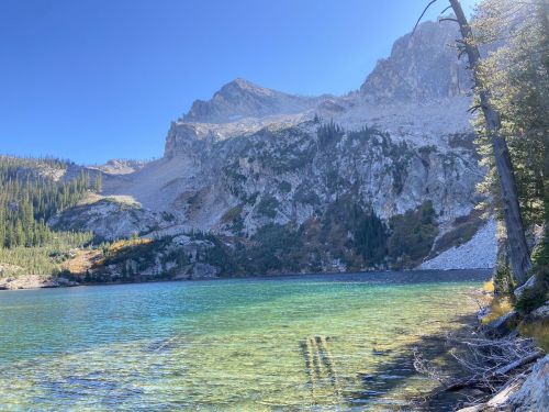 A serene mountain lake surrounded by rocky cliffs and lush greenery under a clear blue sky.