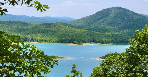 Views of Lake Moomaw, the clearest lake in VA, framed by lush trees with rolling hills in the distance.