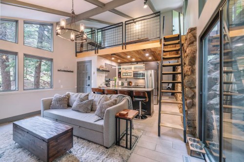 Cozy living area with a sofa, wooden coffee table, and a lofted kitchen space, surrounded by large windows and natural light.