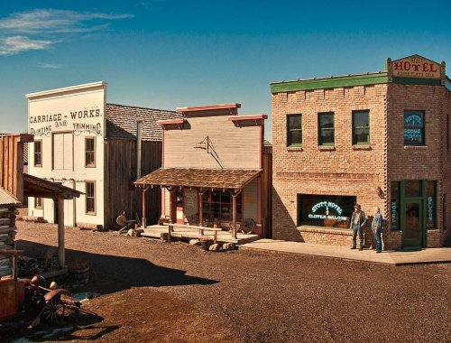 A western-style town with vintage buildings, including a hotel and saloon, under a clear blue sky.