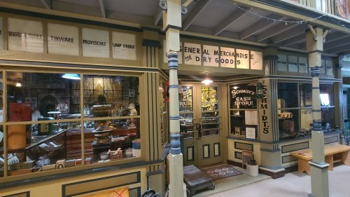 A vintage storefront displaying "General Merchandise" and "Dry Goods," with various items visible through the windows.