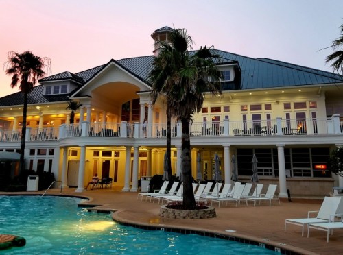 A luxurious pool area with lounge chairs, palm trees, and a grand building at sunset.