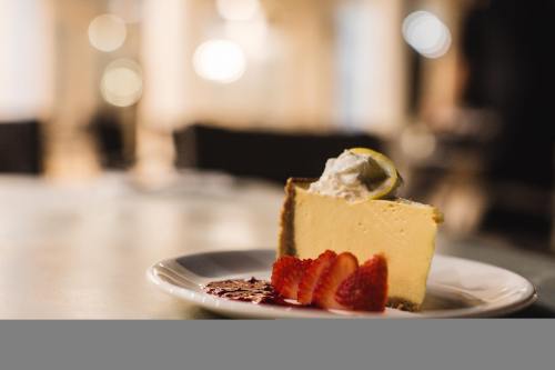 A slice of cheesecake topped with whipped cream and a lime wedge, served with fresh strawberries on a white plate.