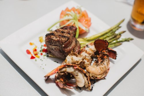 A gourmet plate featuring grilled steak, lobster, asparagus, and a tomato garnish.