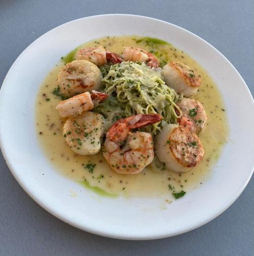 A plate of shrimp and scallops served over pasta with a light sauce and garnished with herbs.