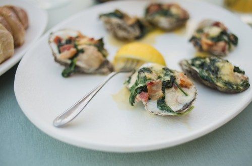 A plate of baked oysters topped with spinach and bacon, served with a lemon wedge.