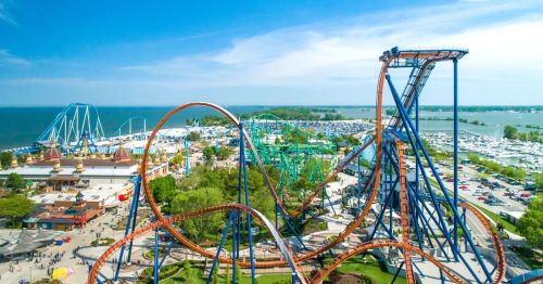 Aerial view of a vibrant amusement park featuring roller coasters, rides, and a scenic waterfront.