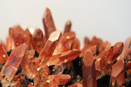 Close-up of vibrant orange crystals with pointed tips, reflecting light against a neutral background.