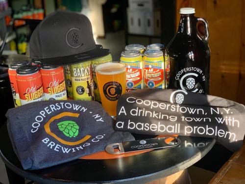 A display of craft beers, a growler, a pint, and merchandise from Cooperstown Brewing Co. with a baseball theme.