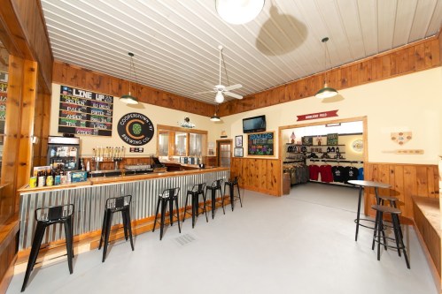 Interior of a brewery with a wooden bar, seating, and a menu board. Merchandise displayed on the walls.