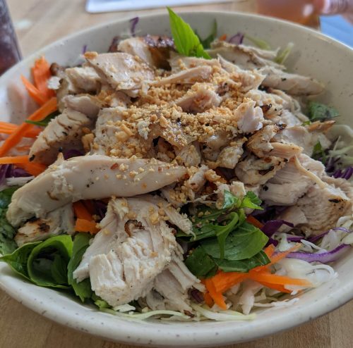 A bowl of salad topped with grilled chicken, mixed greens, carrots, and crushed peanuts.