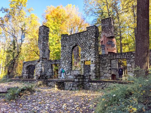Stone ruins surrounded by colorful autumn trees, with two people exploring the site.