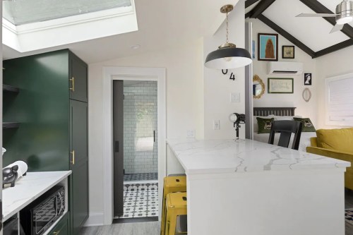 Modern kitchen with green cabinets, white marble countertop, and a skylight, leading to a cozy living area.