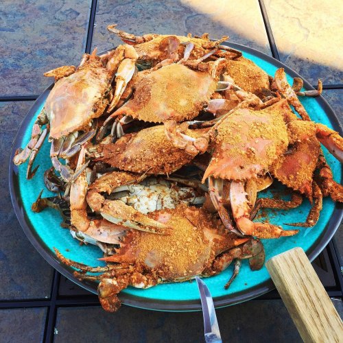 A vibrant blue plate filled with seasoned crabs, ready to be served, on a textured table surface.