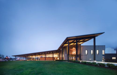 Modern building with a large overhanging roof, surrounded by green grass and a cloudy sky.