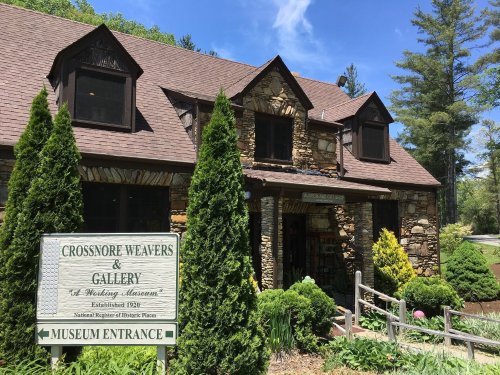 Stone building with a sign for Crossnore Weavers & Gallery, surrounded by greenery and trees on a sunny day.