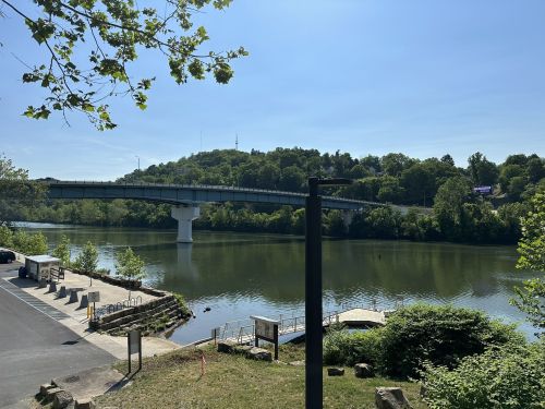 A serene river scene featuring a bridge, lush greenery, and a clear blue sky reflecting on the water.