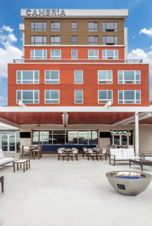 Exterior view of the Cambria hotel, featuring a modern design and outdoor seating area with a fire pit.