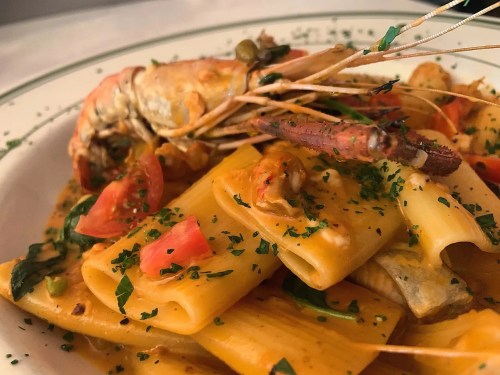 A close-up of pasta with shrimp, tomatoes, and herbs, served on a white plate with a green rim.
