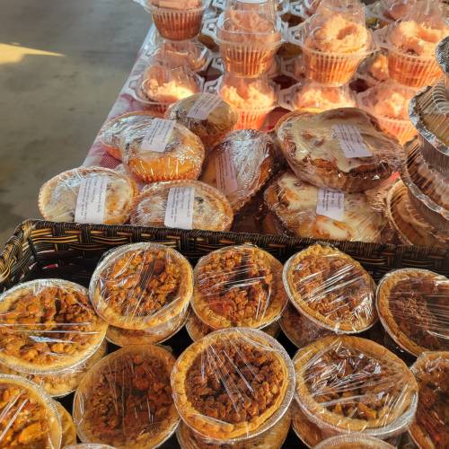 A display of assorted baked goods, including pies and cupcakes, wrapped in plastic on a table.