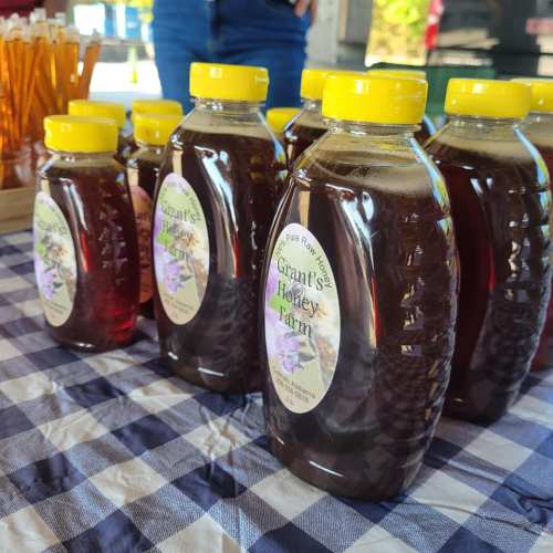 Bottles of honey with yellow caps on a checkered tablecloth, labeled "Grant Honey Farm."