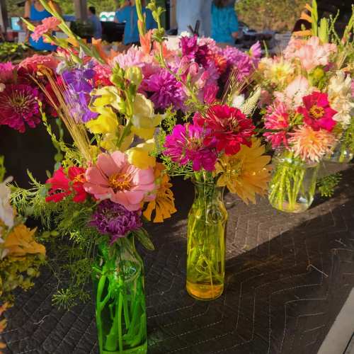 Colorful flower arrangements in glass bottles on a table, featuring a variety of blooms and greenery.