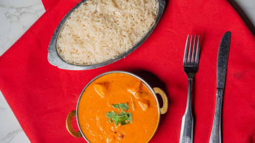 A bowl of creamy orange curry with chicken, garnished with cilantro, served alongside a portion of fluffy white rice.