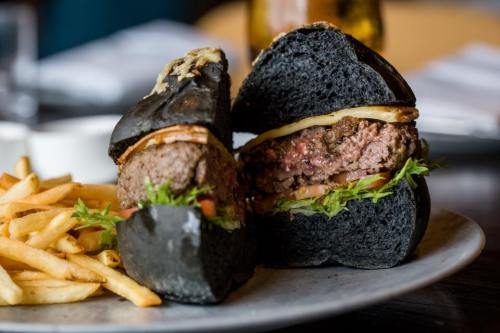 A gourmet burger with a black bun, lettuce, tomato, and onion, served with a side of golden fries.