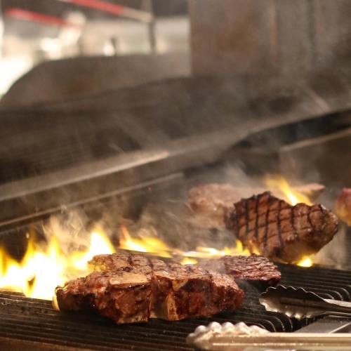 Steaks sizzling on a grill with flames and smoke rising, showcasing a delicious cooking process.