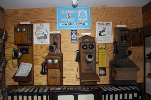A display of vintage wall-mounted telephones and related signage in a wooden setting.