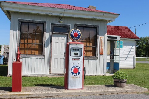 A vintage gas station with a classic gas pump and a small building, set against a clear blue sky.