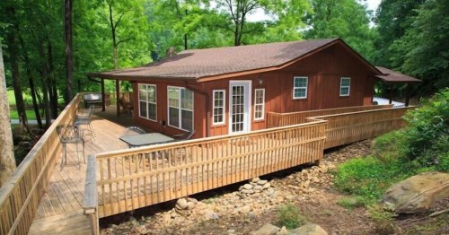 A wooden cabin surrounded by trees, featuring a spacious deck and outdoor seating area.