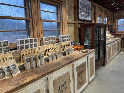 A rustic shop interior with wooden counters displaying packaged goods and a glass display case. Natural light from windows.