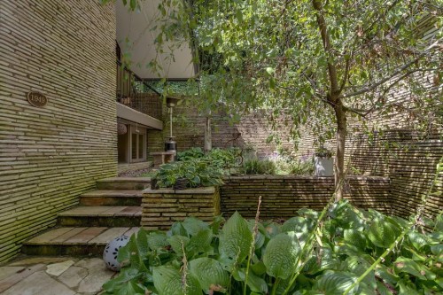 A serene garden with stone walls, lush greenery, and a staircase leading to a shaded area.