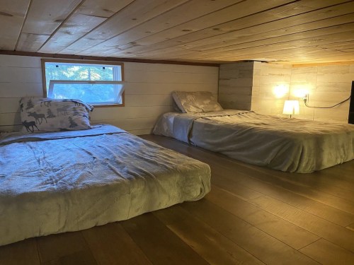 Cozy loft bedroom with two beds, wooden walls, and a small window letting in natural light.
