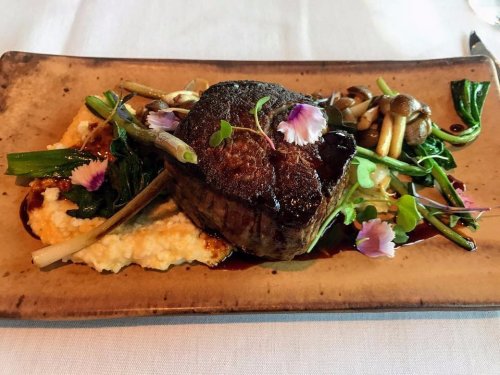 A beautifully plated steak on a bed of creamy polenta, garnished with greens and edible flowers.
