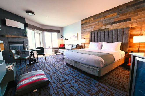 Cozy hotel room featuring a king bed, seating area, desk, and large windows with natural light. Modern decor with wood accents.