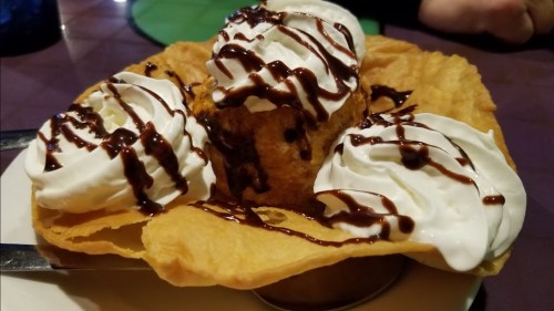 A dessert featuring a crispy shell filled with ice cream, topped with whipped cream and drizzled with chocolate sauce.