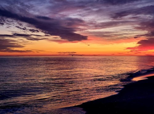 A vibrant sunset over a calm ocean, with colorful clouds reflecting on the water's surface.