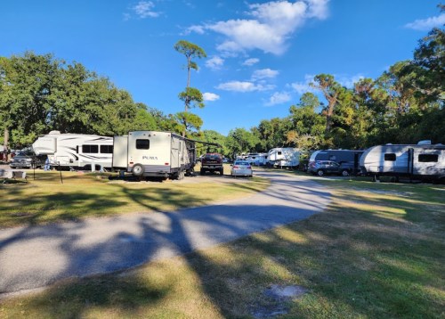 A sunny RV park with several parked trailers and a winding road surrounded by trees and blue skies.