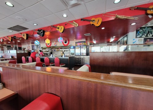 A colorful diner interior with red accents, guitars hanging from the ceiling, and a counter with seating.