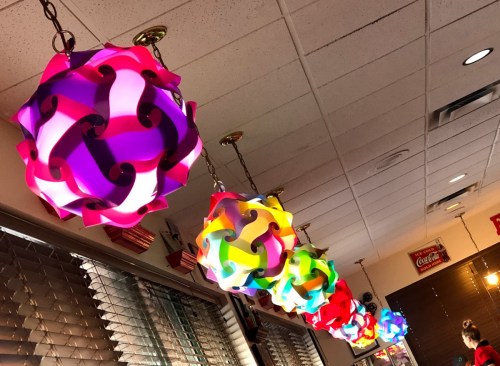 Colorful, decorative pendant lights hang from the ceiling in a restaurant, creating a vibrant atmosphere.